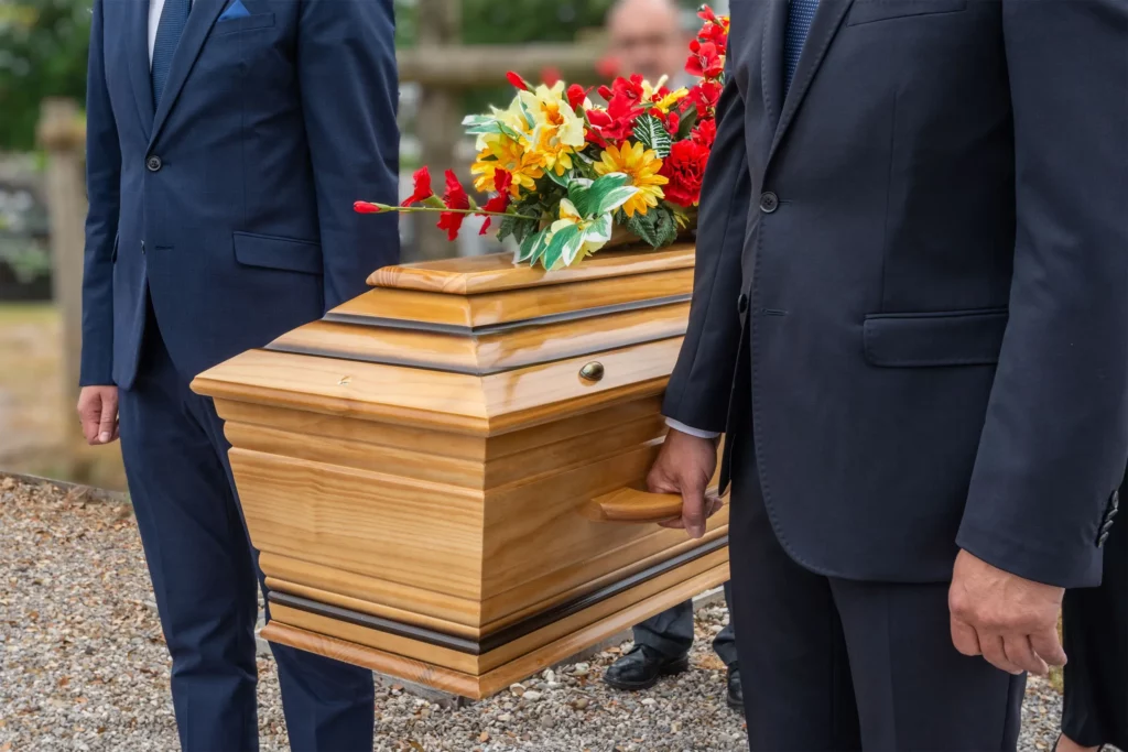 Porteurs funéraires en costume transportant un cercueil en bois fleuri.