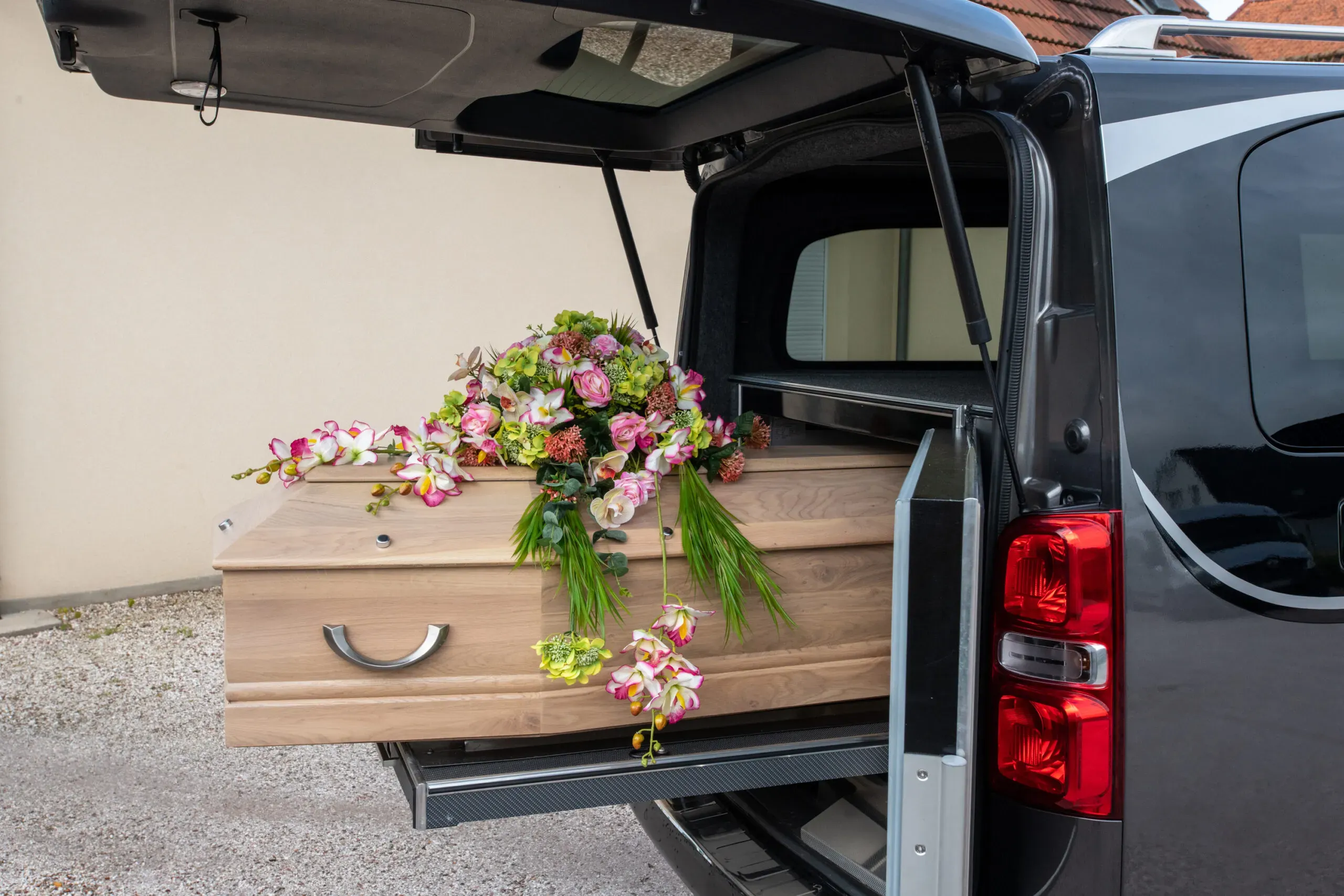 Cercueil en bois clair orné de fleurs installé dans un corbillard.